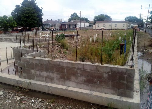 Weeds grow in the fenced-off foundation laid three years ago for Martin Wine Cellar on Baronne Street. (Robert Morris, UptownMessenger.com)