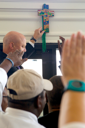 Mayor Mitch Landrieu hangs a cross over the doorway of Cafe Reconcile as guests put up their hands in prayer. (Sabree Hill, UptownMessenger.com)