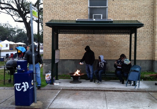Revelers awaiting Rex on Mardi Gras Day underneath the bus stop at Freret and Napoleon fuel their fire in an effort to keep warm. (Photo by Jean-Paul Villere for UptownMessenger.com)