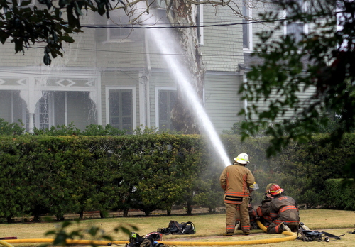 Firefighters spray water from an adjacent yard.  (Robert Morris, UptownMessenger.com)