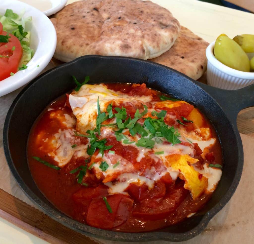 Shaksuka of Eggs Poached in Red Pepper and Tomato Sauce, with Tahini, Pita, and Salad. (Kristine Froeba)